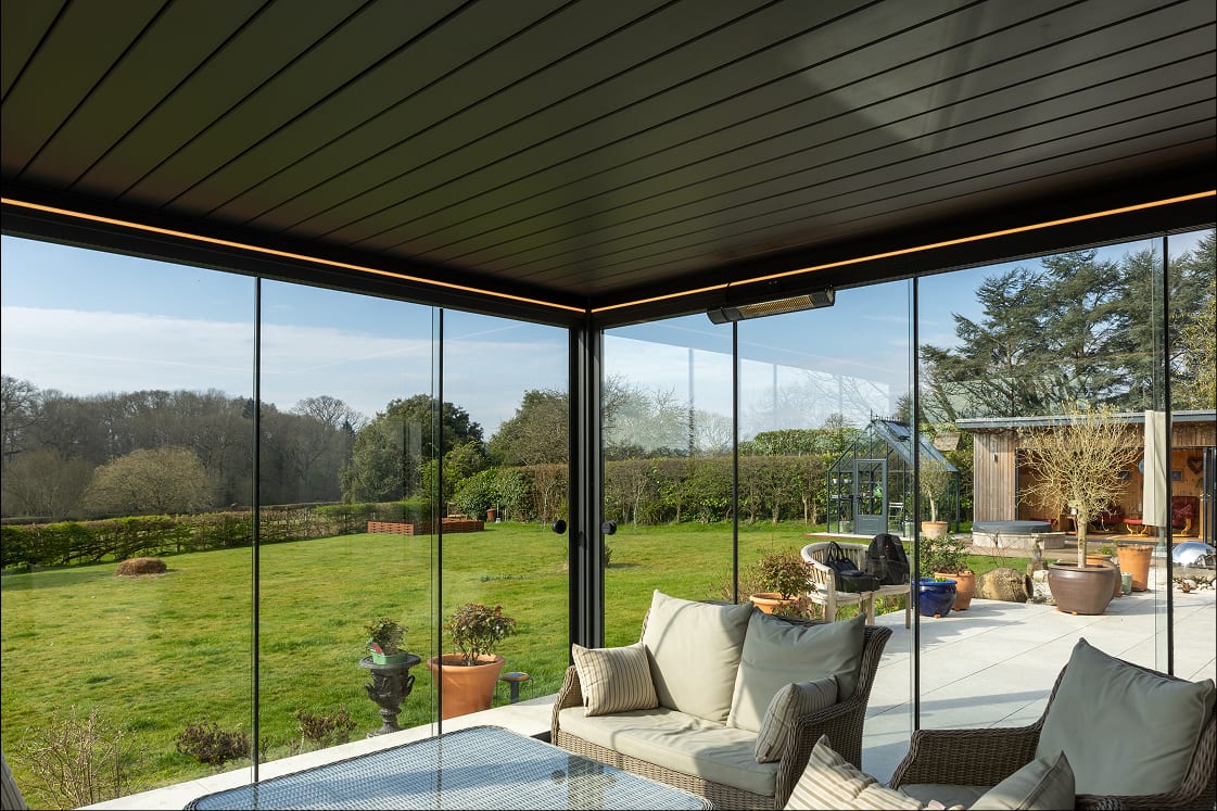 Pergola bioclimatique avec store vertical déployé sur un côté et paroi vitrée sur un autre, terrasse automne mi-saison