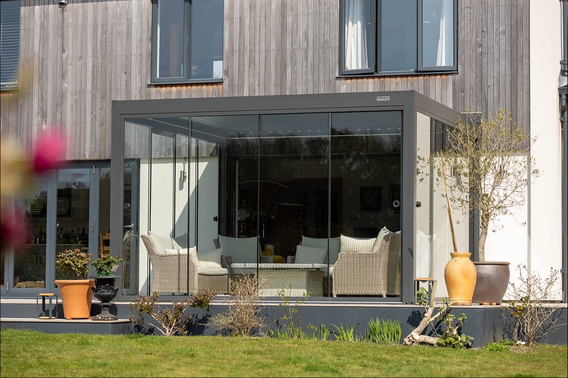Pergola 4 Pro with Glass Walls partially closed over a UK garden terrace, showing the enclosed-space accessory upgrade in a rainy setting