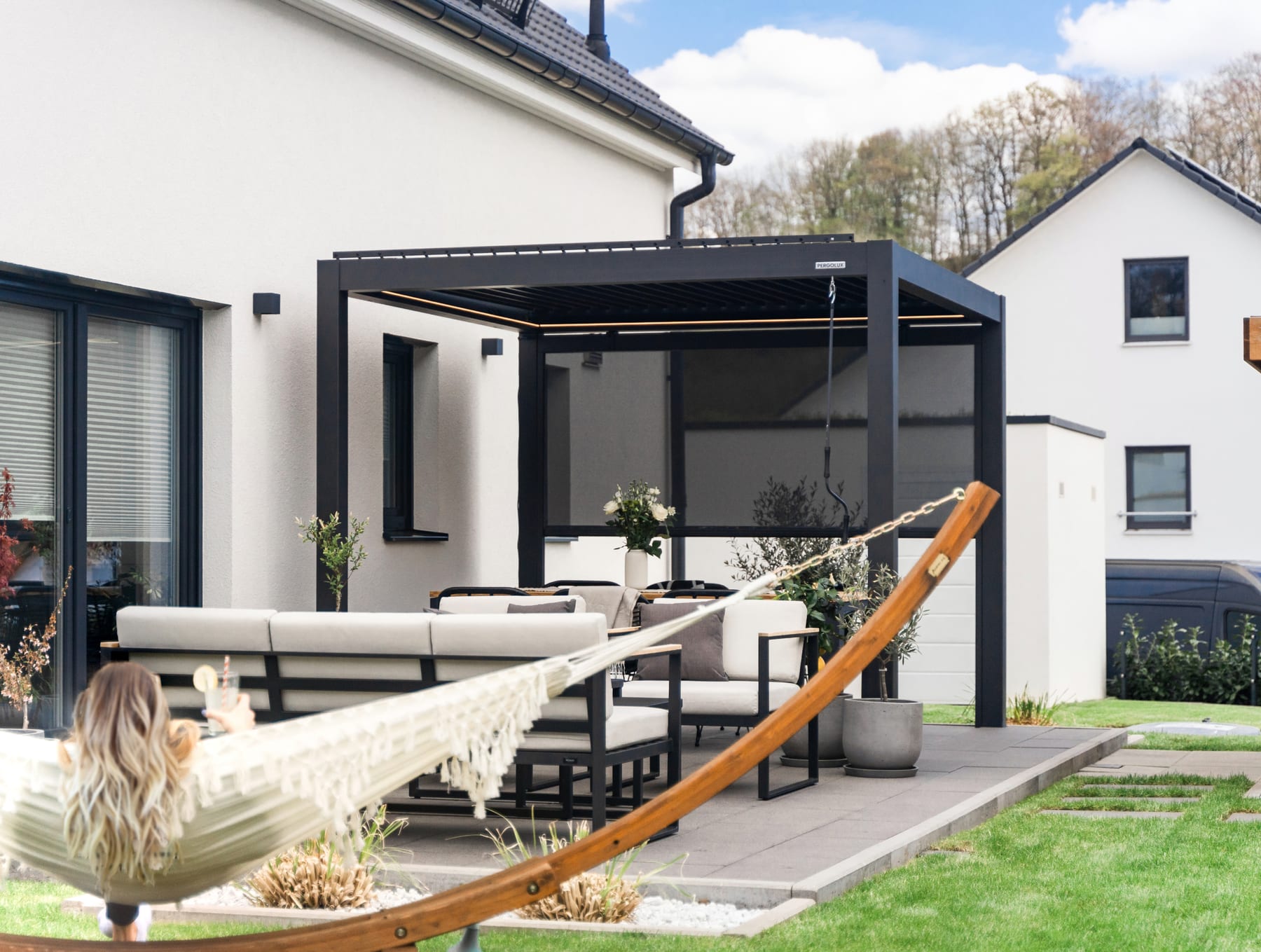 Terrasse française avec pergola bioclimatique aluminium ouverte sur jardin, propriétaire installant une chaise longue par une journée d'automne