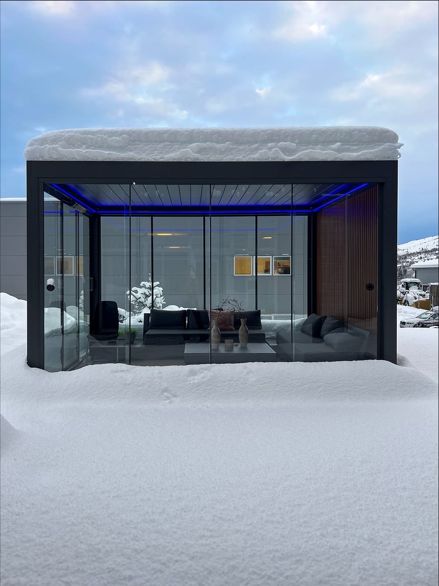 Pergola 4 Pro avec paroi vitrée et store vertical fermés côté vent, soirée d'automne avec lampe chauffante allumée