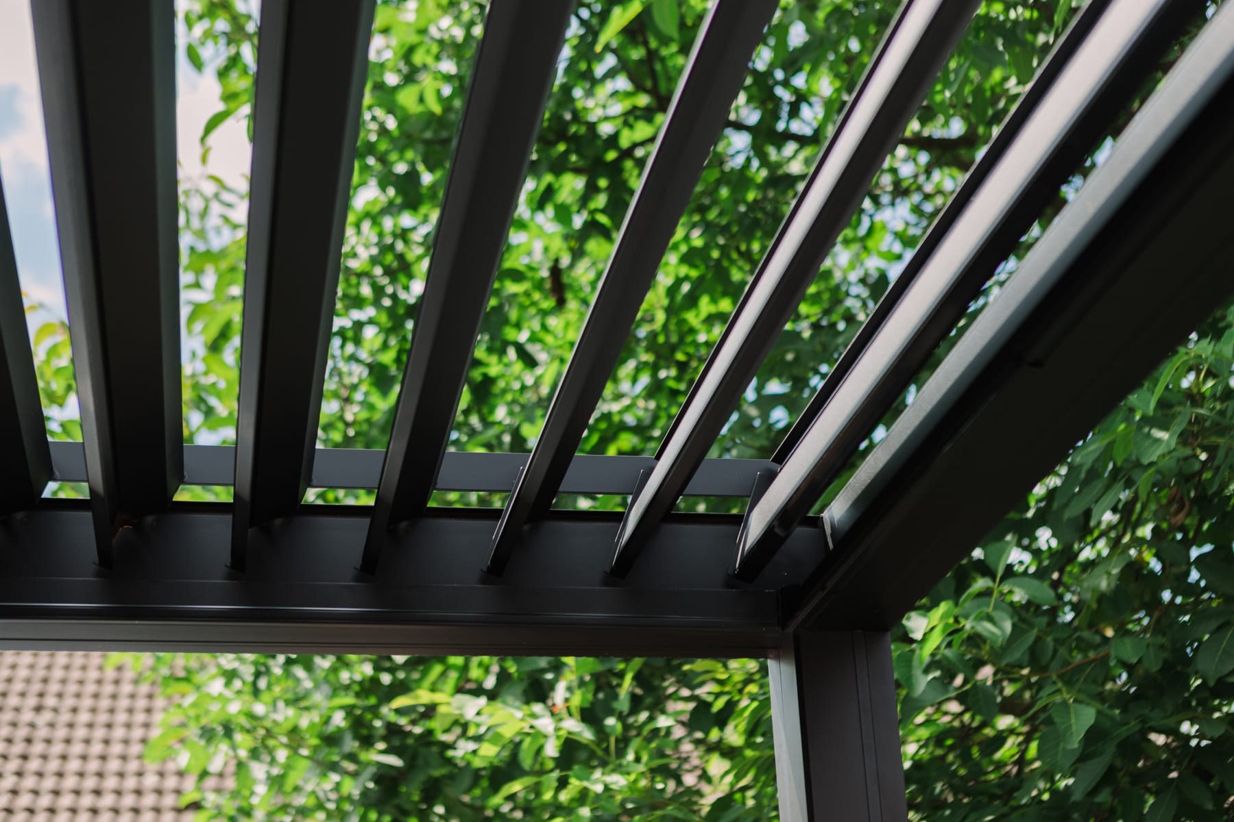 Lames orientables d'une pergola PERGOLUX ouvertes en position cheminée, lumière rasante de fin d'après-midi filtrant entre les lamelles