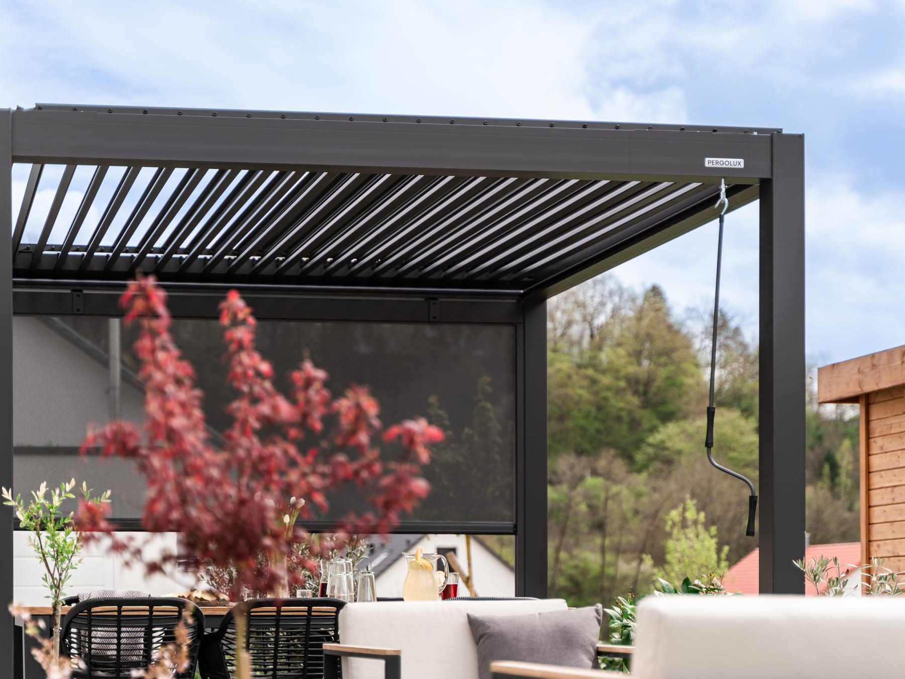Installation d'un rail de store vertical sur pergola aluminium, niveau laser posé sur le rail, deux mains vissant un support