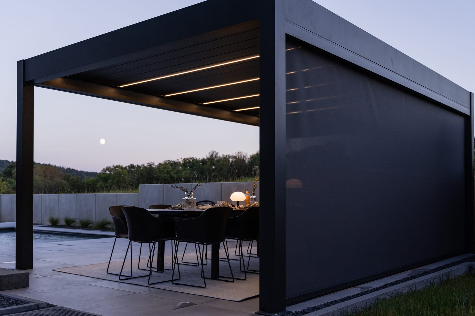 Pérgola com lâminas fechando automaticamente sobre área gourmet enquanto nuvens de chuva tropical se aproximam ao fundo
