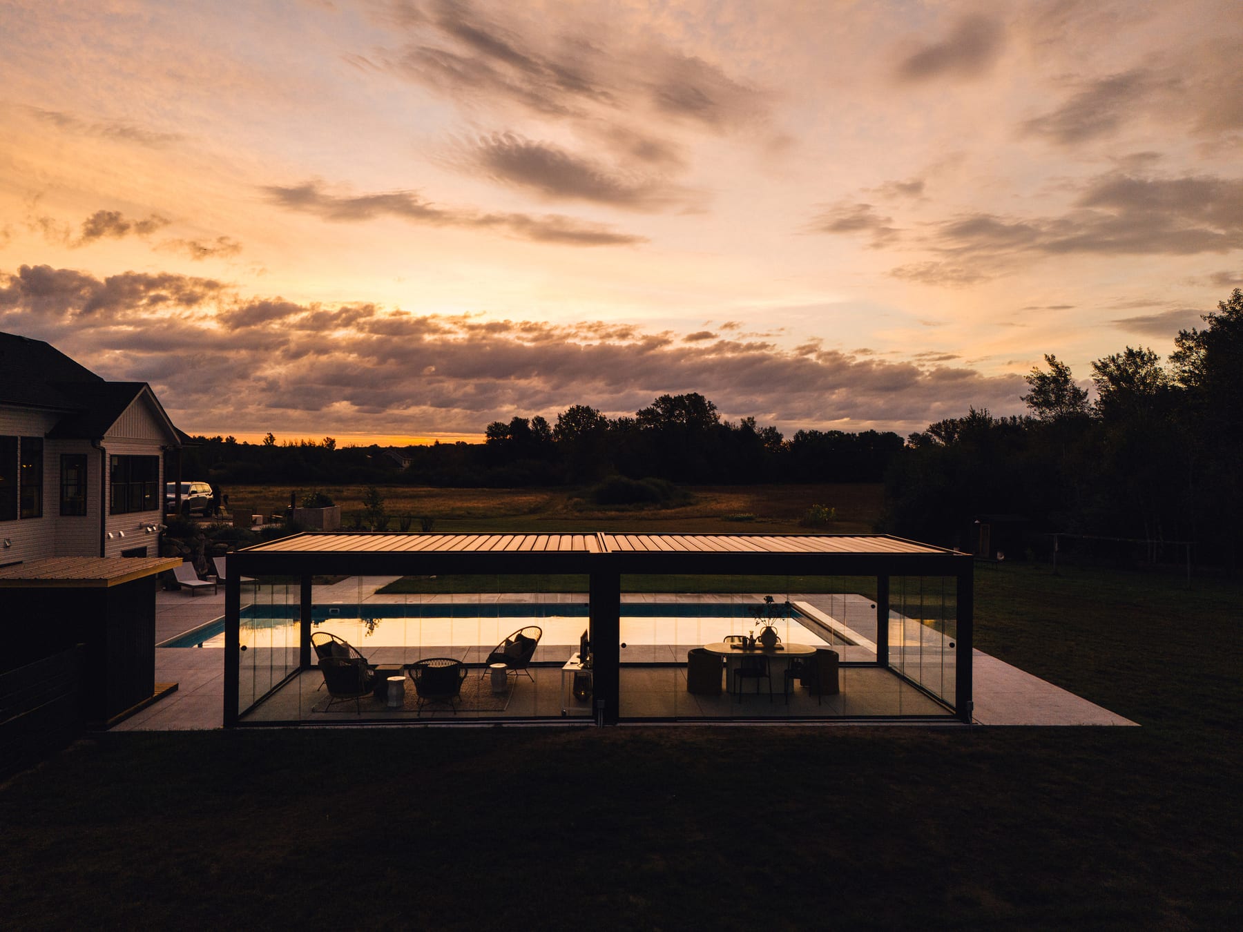 PERGOLUX aluminium pergola with glass wall panels fitted to one side in a finished British garden, evening light